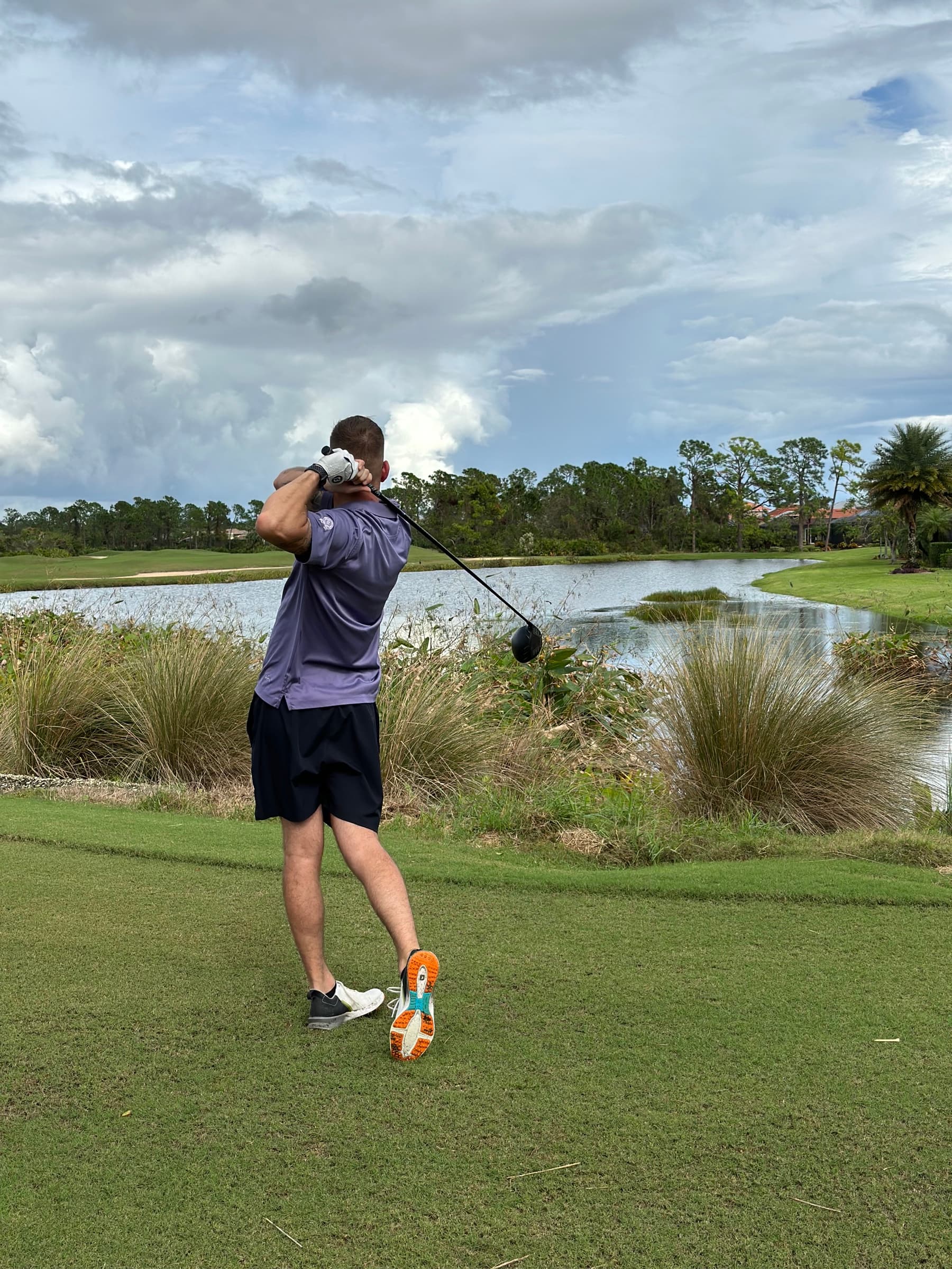 Colin Coughlin holding a driver follow-through beside a lake on the course