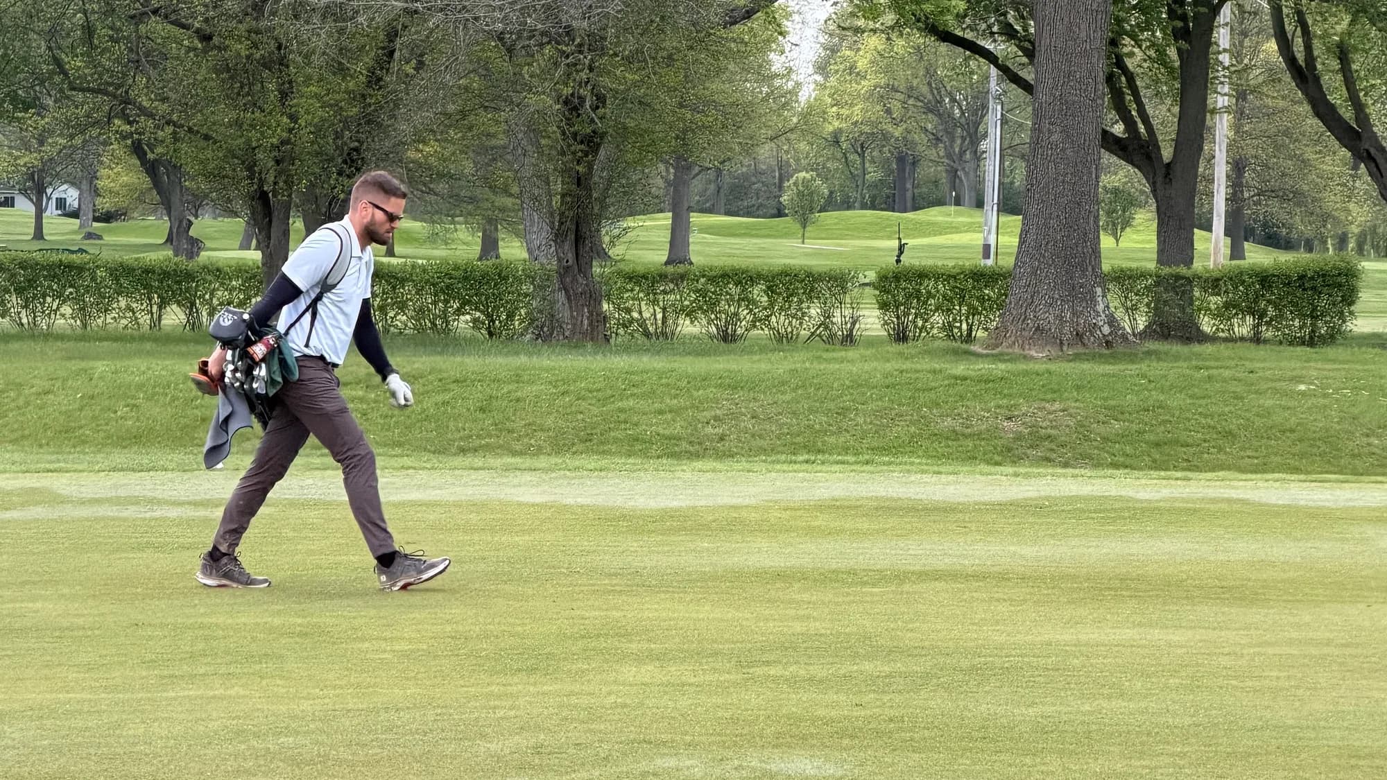 Colin Coughlin walking a tree-lined fairway with his golf bag