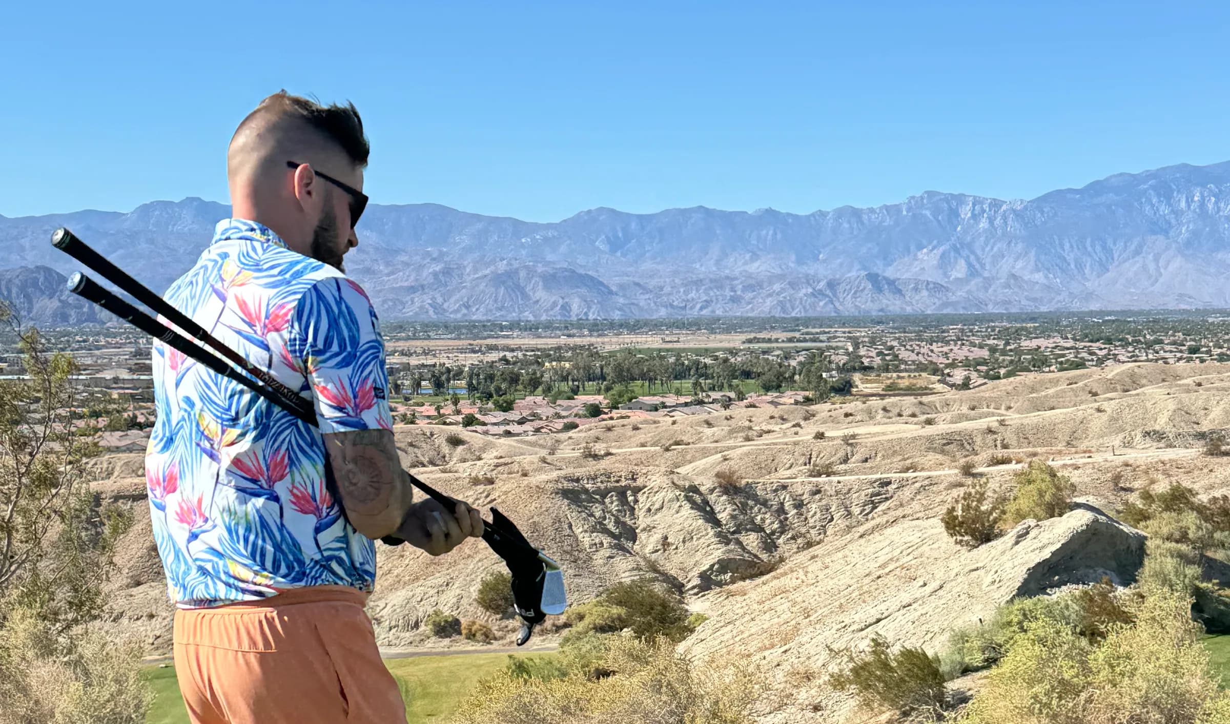 Colin Coughlin standing on an elevated tee box with his clubs over his shoulder, looking out across the course